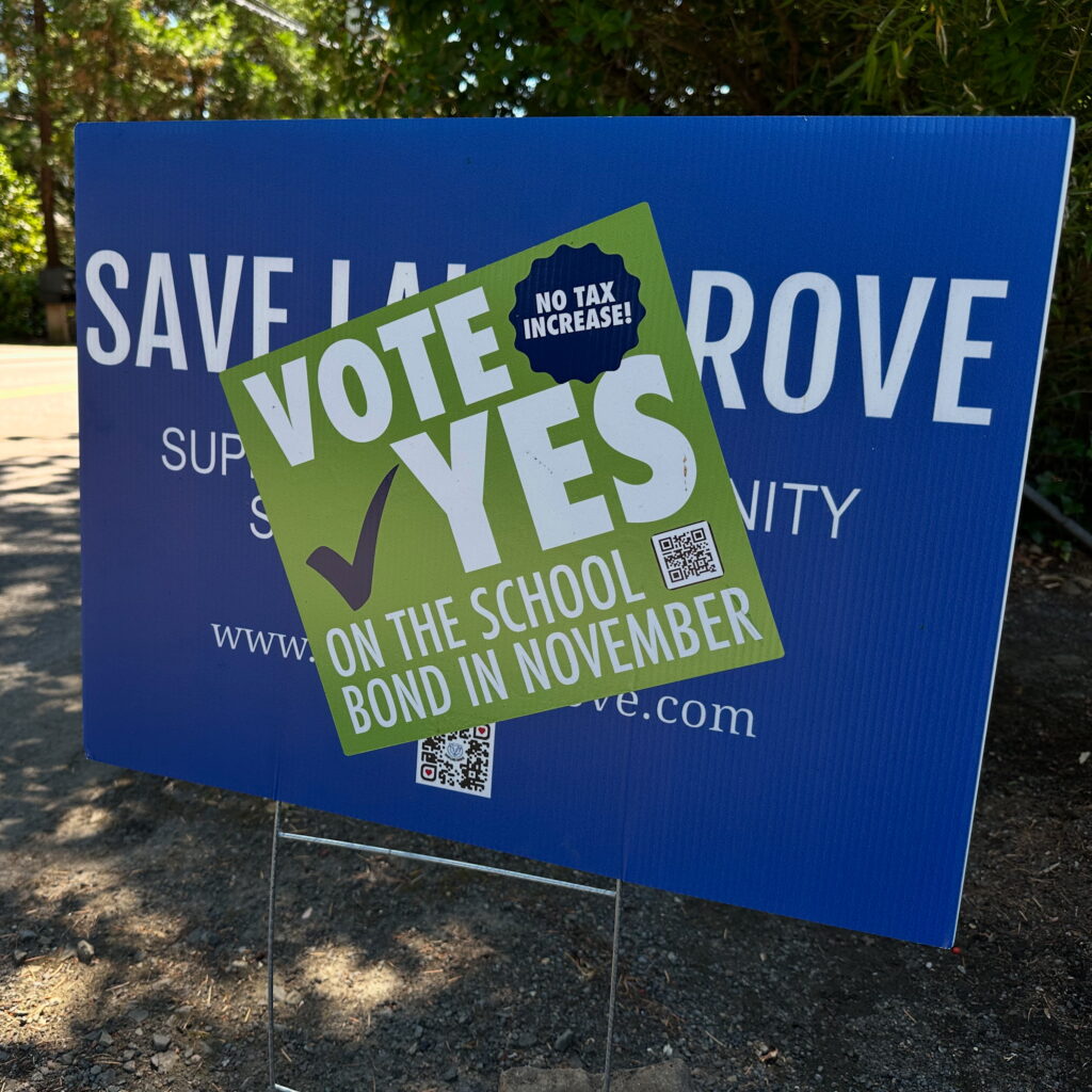 Yard sign with a sticker on top that says "Vote YES on the school bond in November - No Tax Increase!"